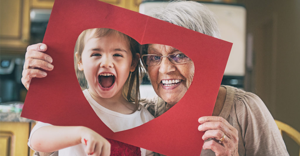 Elderly woman and a little girl holding up a red paper cutout of a heart.